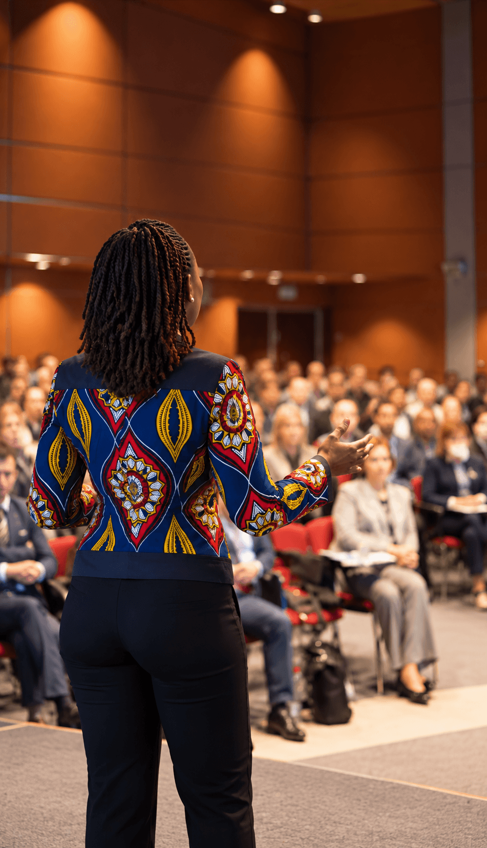 Tebo Shabangu addressing an auditorium audience in a patterned jacket